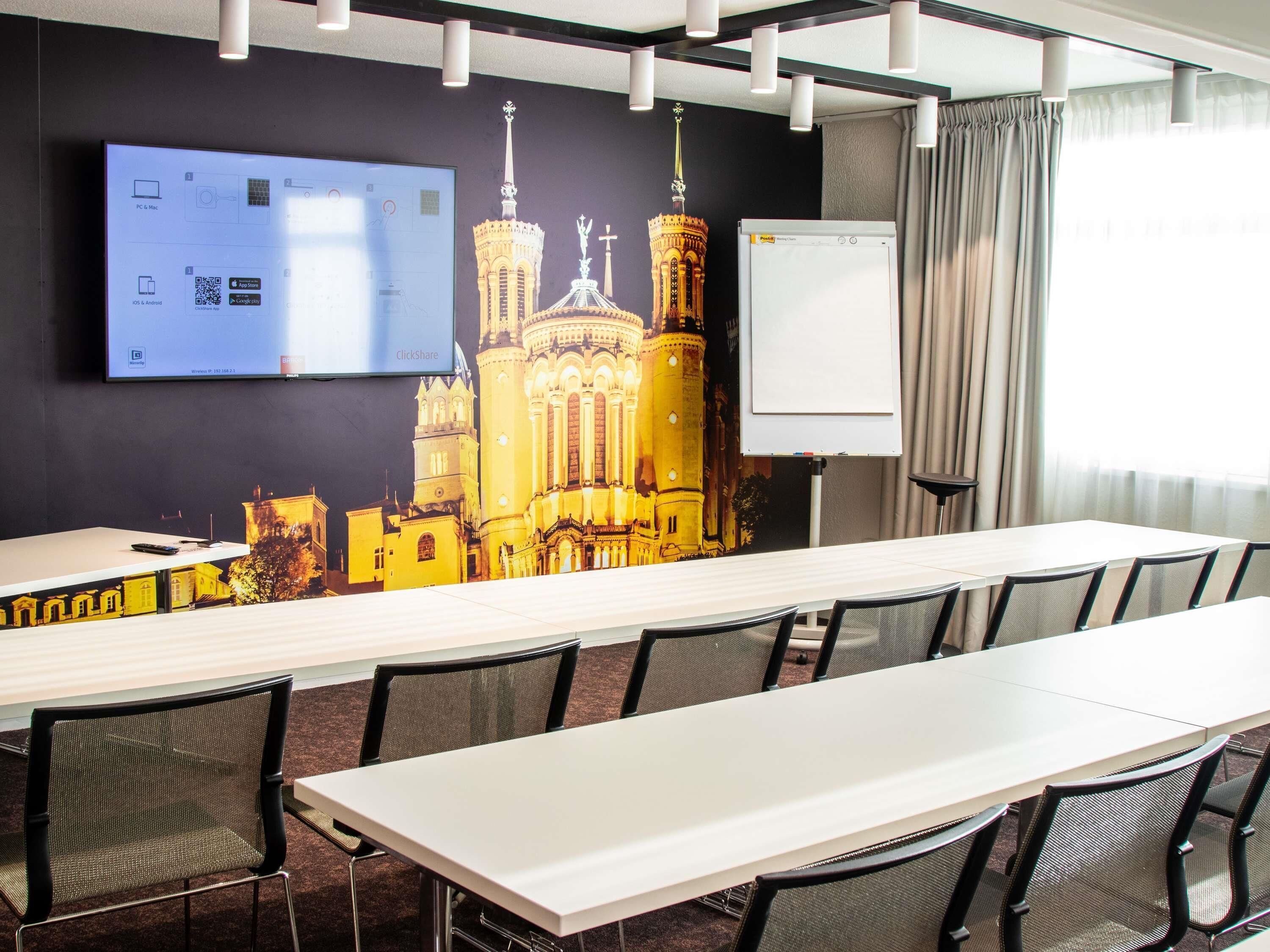 A conference room with a long table, chairs, a projector screen, a whiteboard, and a large wall mural.