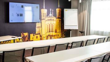 A conference room with a long table, chairs, a projector screen, a whiteboard, and a large wall mural.