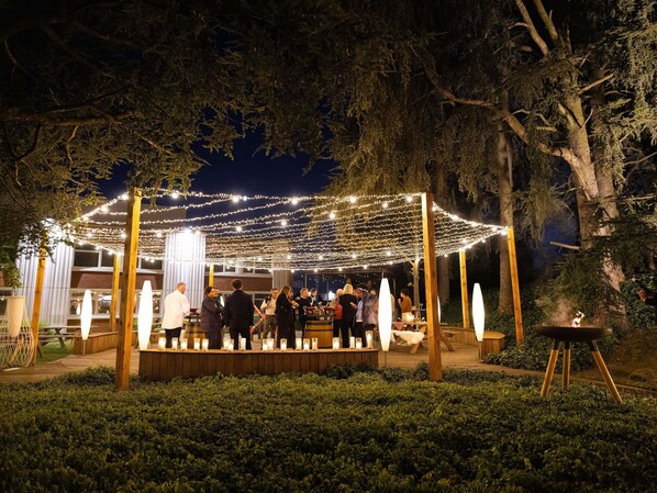 Un espacio para eventos al aire libre con luces colgantes, mesas de madera y velas.
