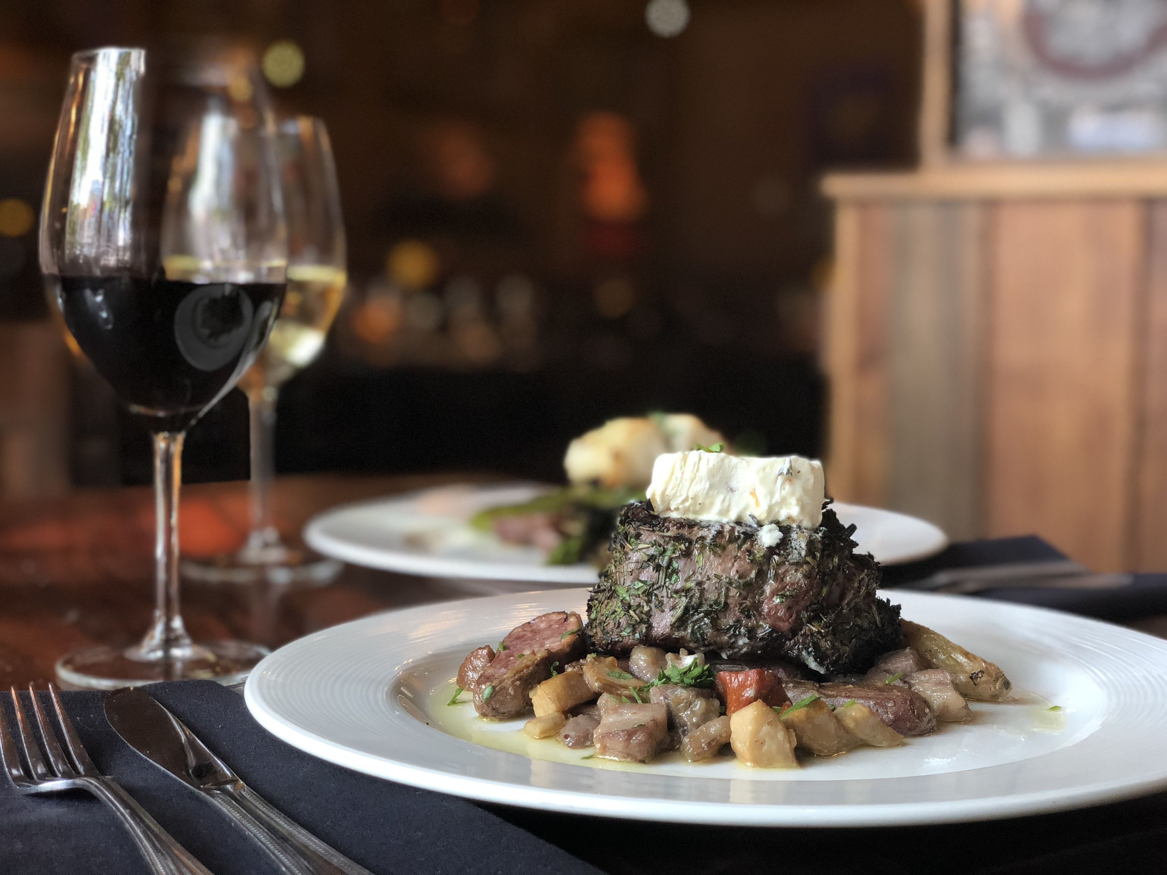 A dining table with plates of food, a glass of red wine, and cutlery.