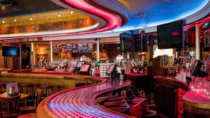 Un bar con un mostrador curvo, taburetes y una variedad de botellas y vasos.