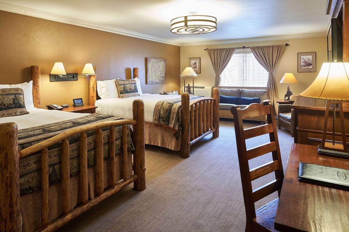 Ein Hotelzimmer mit zwei Betten, einem Holzstuhl, einem Schreibtisch und einer Lampe.