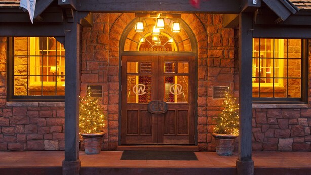 Edificio de piedra con entrada de madera, dos árboles de Navidad en macetas y un letrero sobre la puerta.