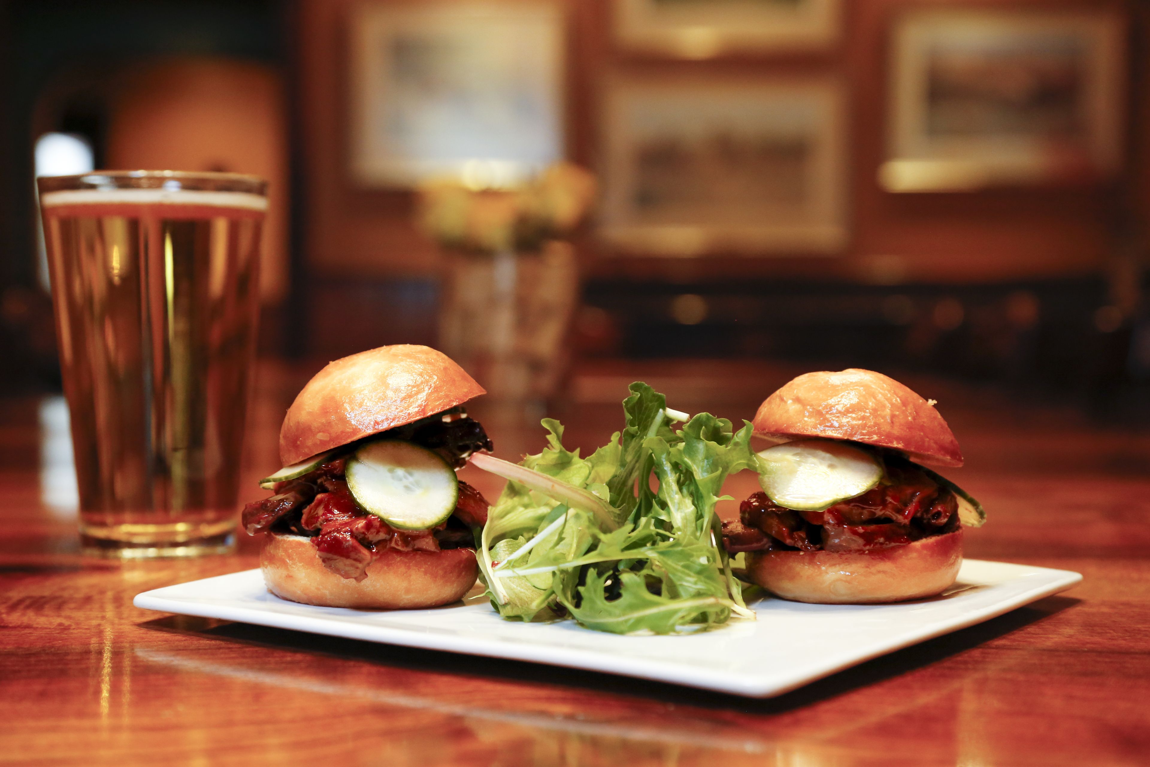 A plate with two sandwiches and a glass of beer on a wooden table.