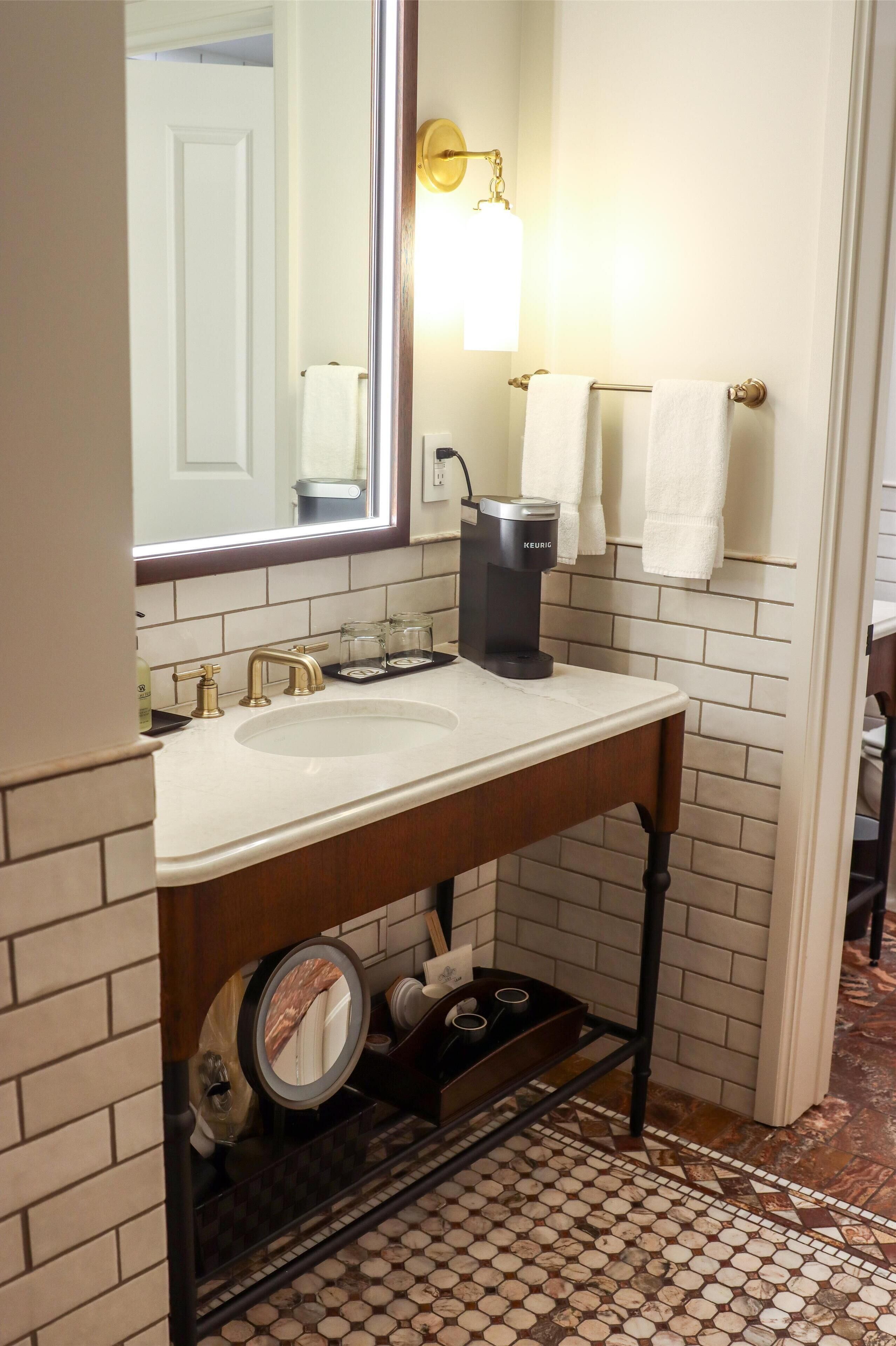 Ein Badezimmer mit weißem Waschbecken, einem Spiegel, einem Handtuchhalter und einer Kaffeemaschine.
