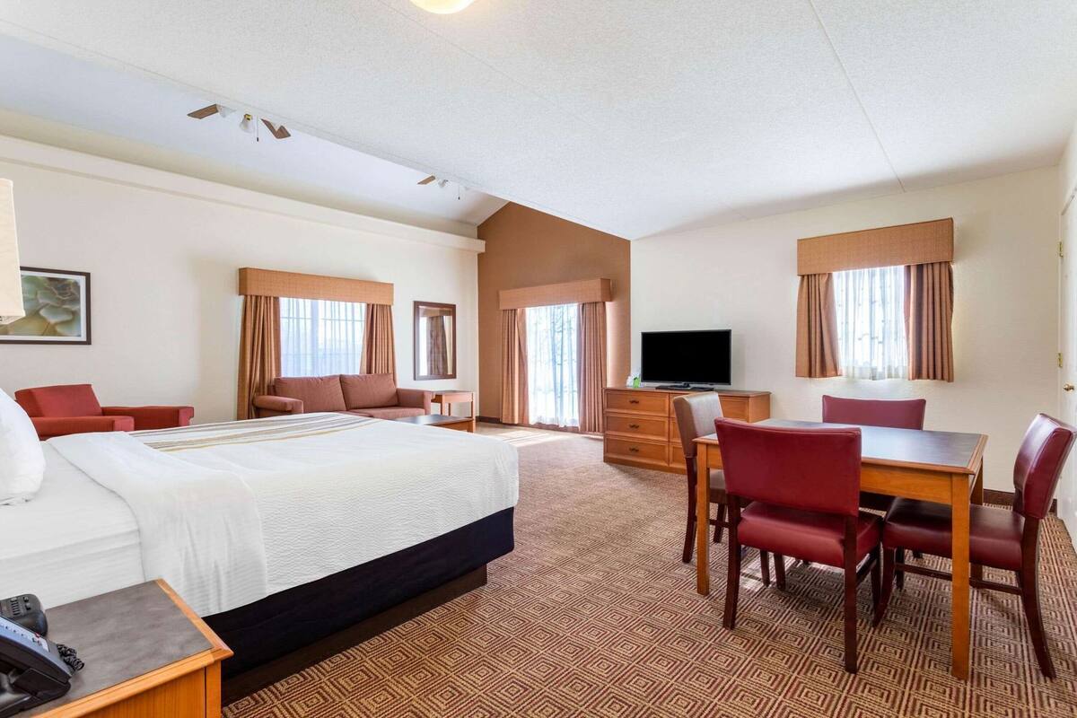 Una habitación de hotel con una cama, un escritorio con silla, un televisor y una mesa de comedor con sillas.