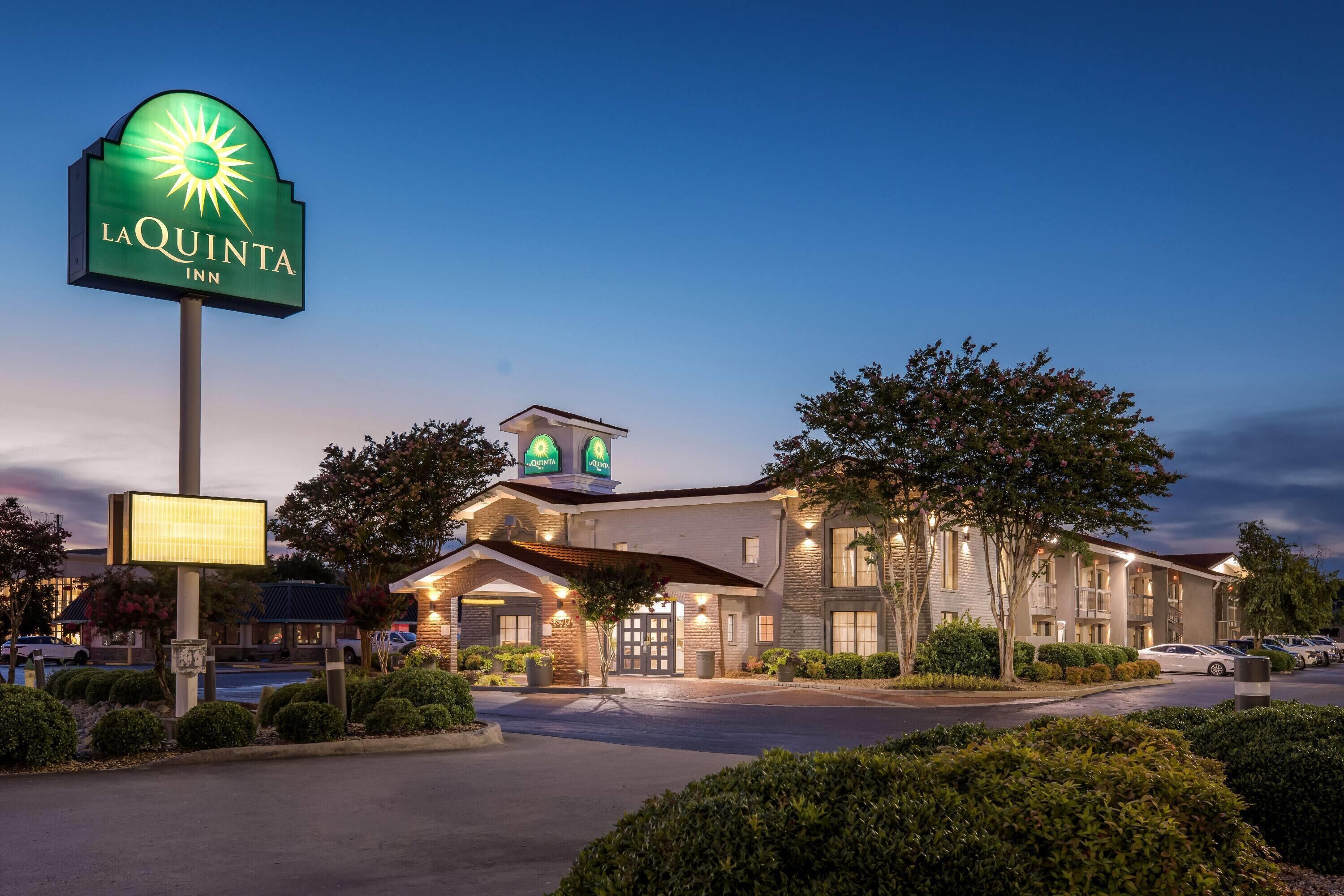 Un hôtel La Quinta Inn doté d’une grande enseigne lumineuse, d’un bâtiment bien éclairé et d’un parking.