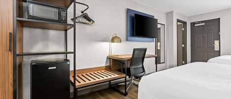 Habitación de hotel con cama, escritorio con silla, microondas, refrigerador, televisor montado en la pared y una puerta.