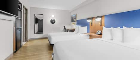 A hotel room with two beds, a desk, a chair, a lamp, and a mirror.