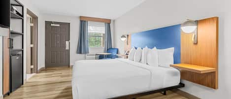 A modern hotel room with a large bed, a desk, and a wardrobe.