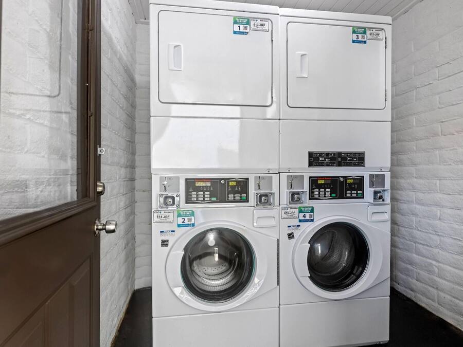 A laundry room with two stacked front-loading washing machines, a dryer, and a door.