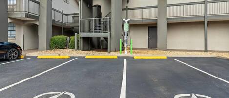 A parking lot with electric vehicle charging stations and a building with a balcony and stairs.