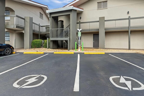 Un estacionamiento con estaciones de carga para vehículos eléctricos y un edificio con balcón y escaleras.