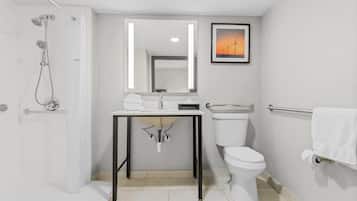 A modern bathroom with a shower, toilet, sink, and a framed picture on the wall.