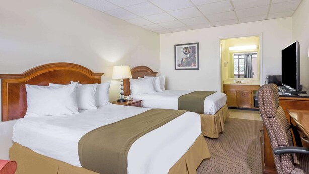 A hotel room with two beds, a desk, a chair, a television, and a window with curtains. - Days Inn by Wyndham Bedford (Bedford)