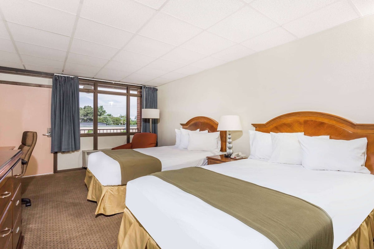 A hotel room with two beds, a desk, a chair, and a window with curtains.