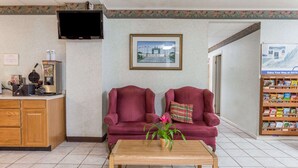 A reception area with a wooden desk, two red armchairs, a coffee table, a television, a framed picture on the wall, and a bookshelf with books. - Days Inn by Wyndham Bedford (Bedford)