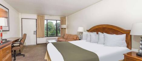 Una habitación de hotel con una cama grande, un escritorio, una silla y una ventana con cortinas.