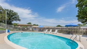 A swimming pool with a wooden fence, lounge chairs, and a covered area with umbrellas. - Days Inn by Wyndham Bedford (Bedford)