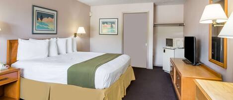 Habitación de hotel con cama, mesitas de noche, escritorio, televisor, microondas y cuadros en las paredes.