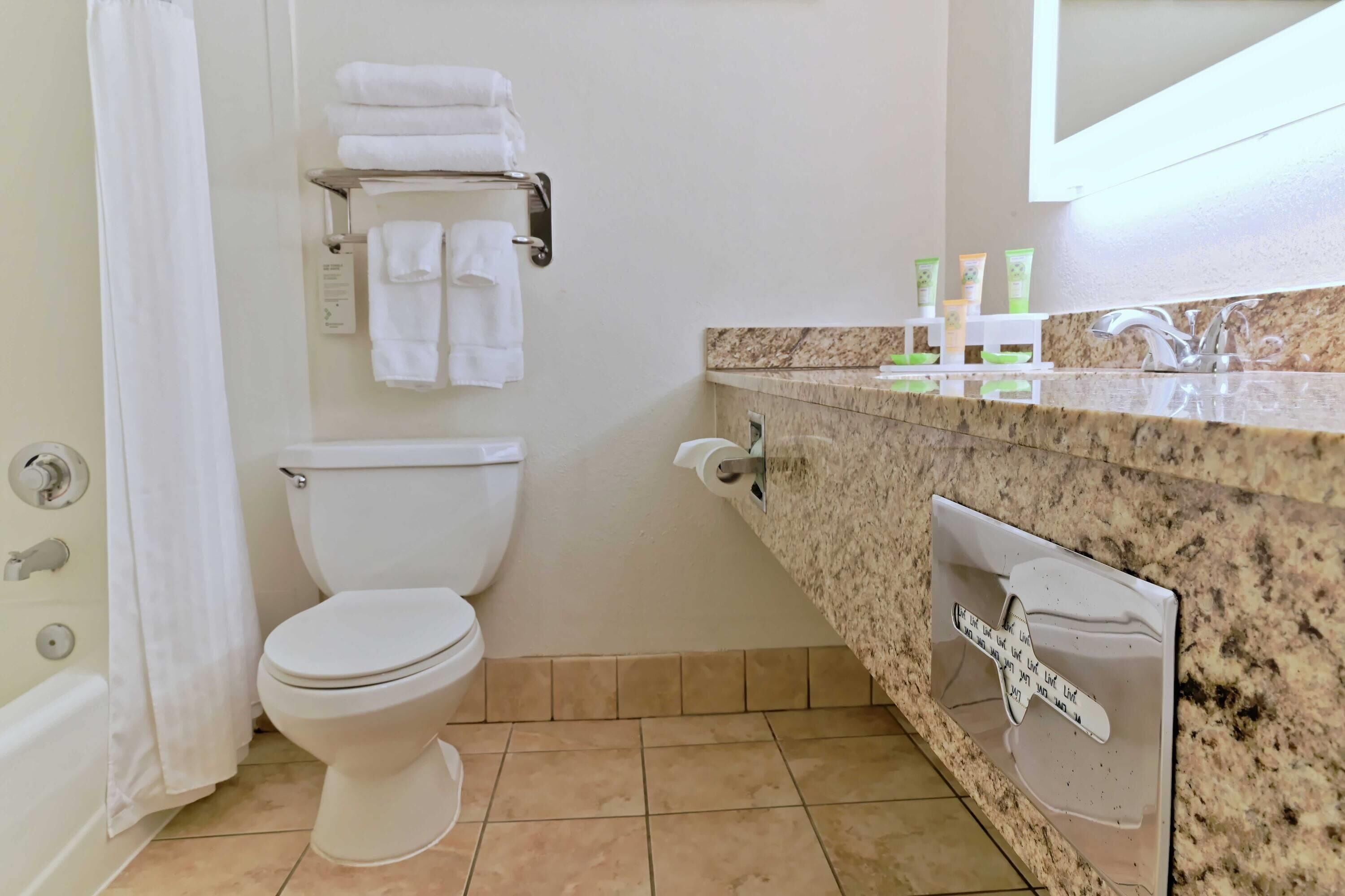 A bathroom with a toilet, a towel rack with folded towels, a sink with a mirror, and toiletries on the countertop.