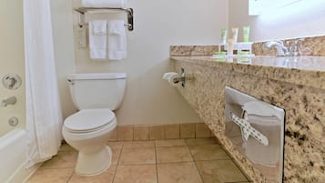 A bathroom with a toilet, a towel rack with folded towels, a sink with a mirror, and toiletries on the countertop.