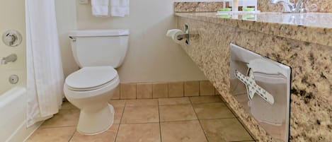 A bathroom with a toilet, a towel rack with folded towels, a sink with a mirror, and toiletries on the countertop.