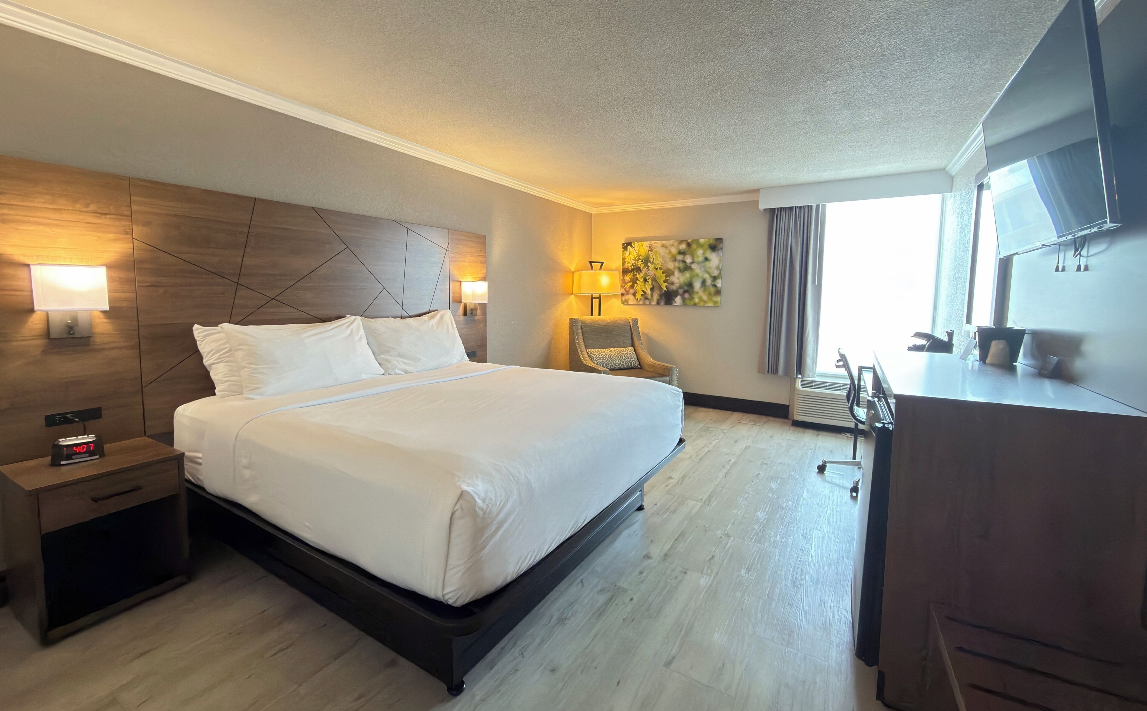 Una habitación de hotel con cama, lámparas de noche, una silla, escritorio y televisor.