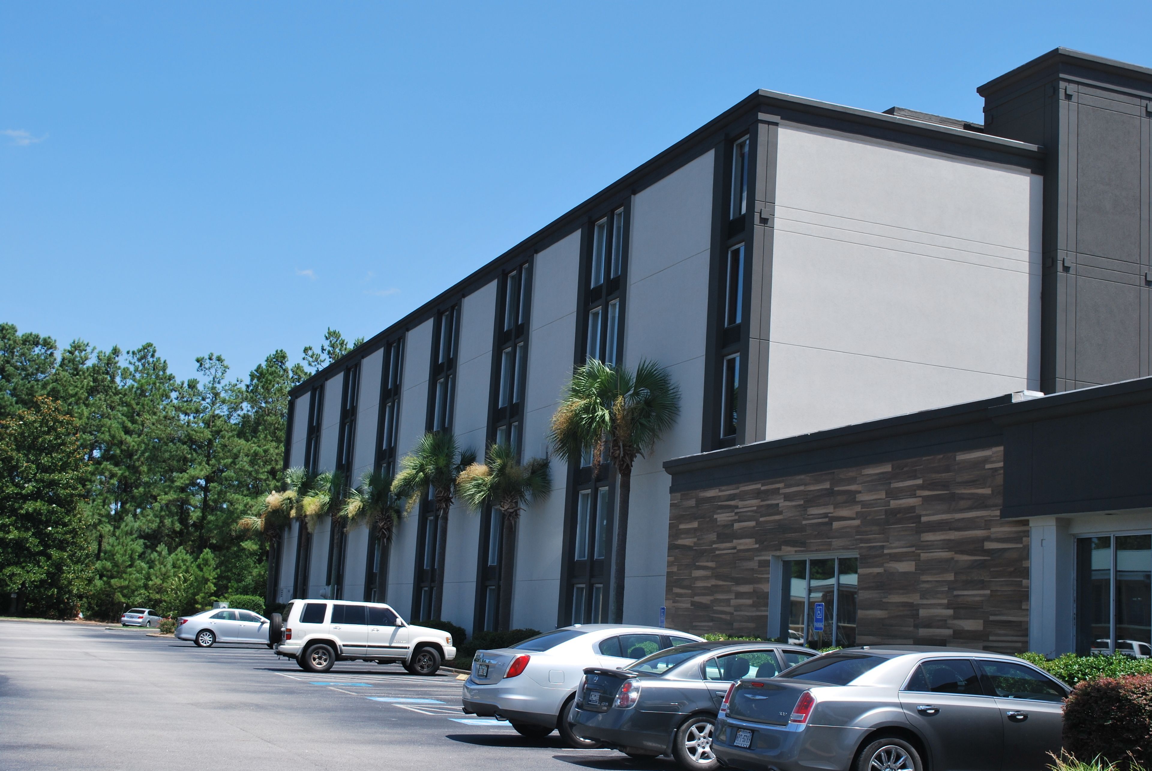 A modern building with a parking lot, featuring a mix of cars and a white SUV.