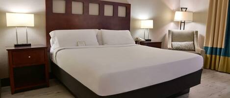 Habitación de hotel con una cama grande, dos mesitas de noche, una silla y una lámpara.