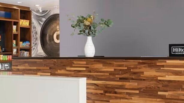 A reception desk with a wooden panel design, a white vase with dried flowers, and a sign reading "Hilton HONOR". - Hampton Inn by Hilton Clanton (Clanton)