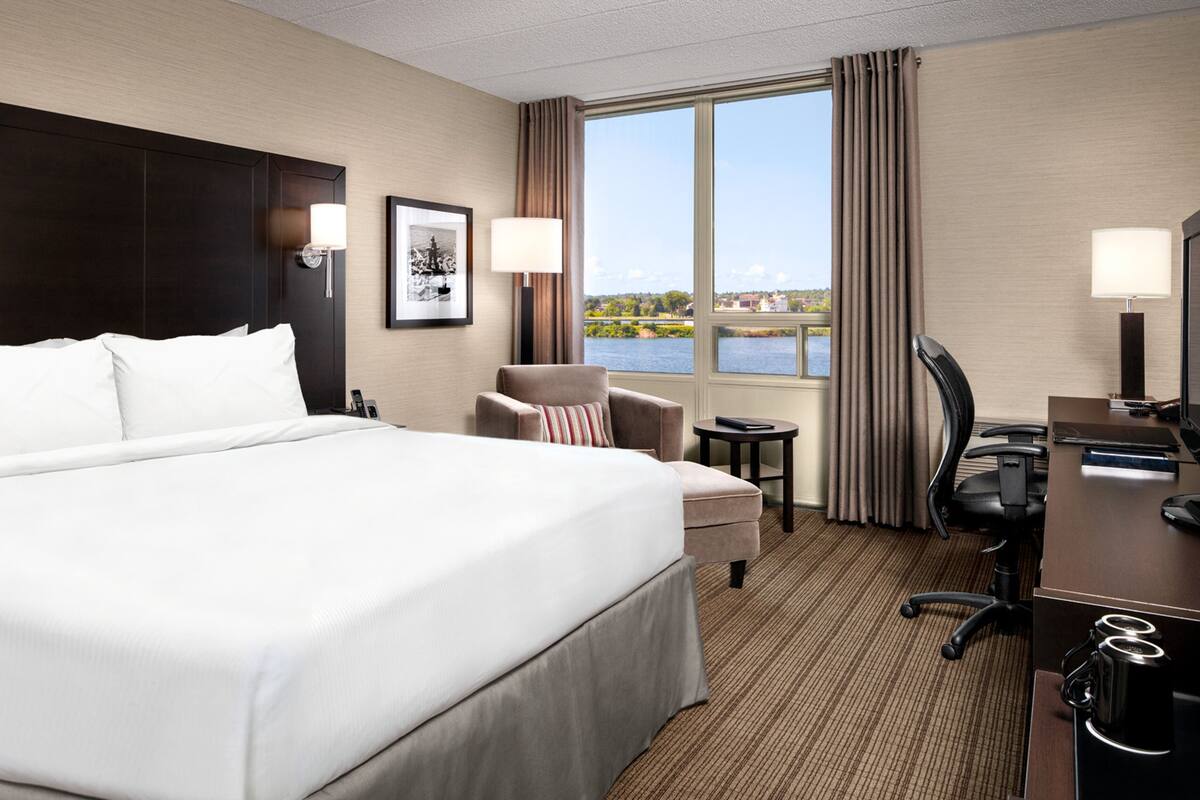 A hotel room with a large bed, a desk, a chair, and a view of a body of water through the window.