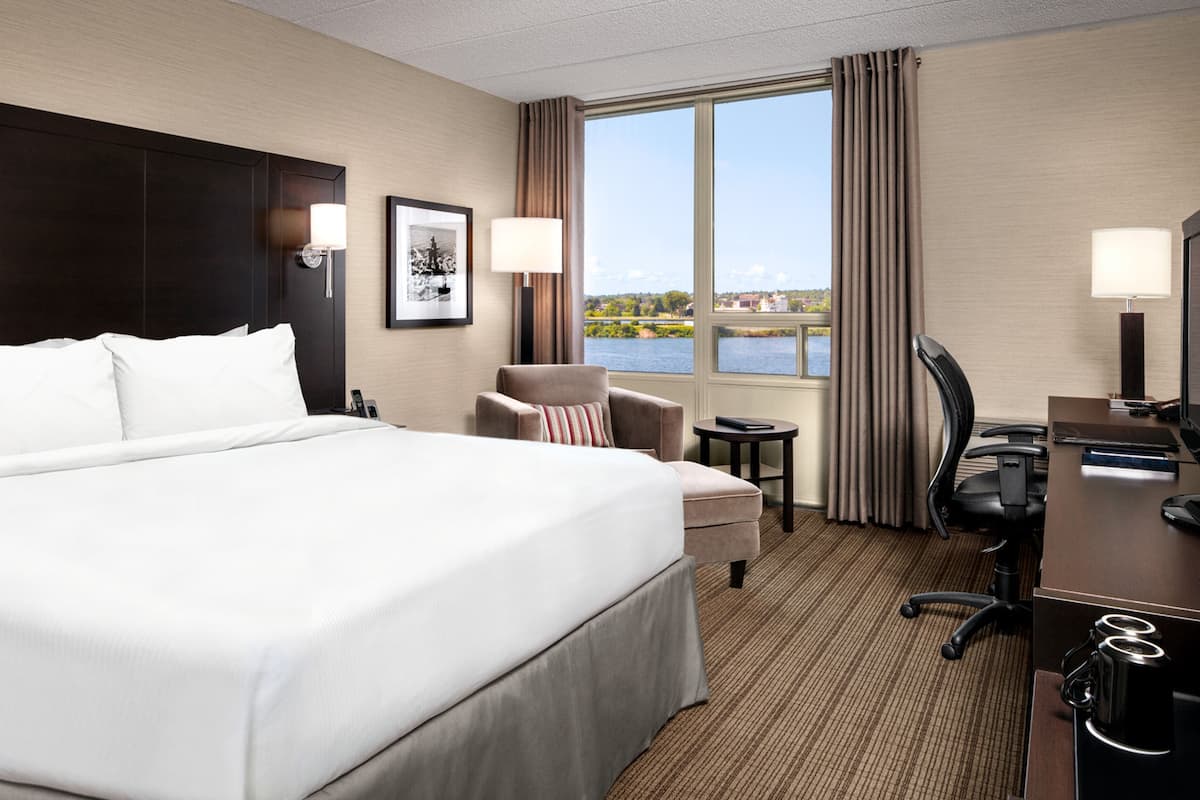 A hotel room with a large bed, a desk, a chair, and a view of a body of water through the window.