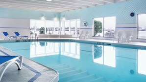An indoor swimming pool with clear blue water, sunlit by large windows, surrounded by lounge chairs and a tiled deck. - Delta Hotels by Marriott Sault Ste. Marie Waterfront (Sault Ste. Marie)