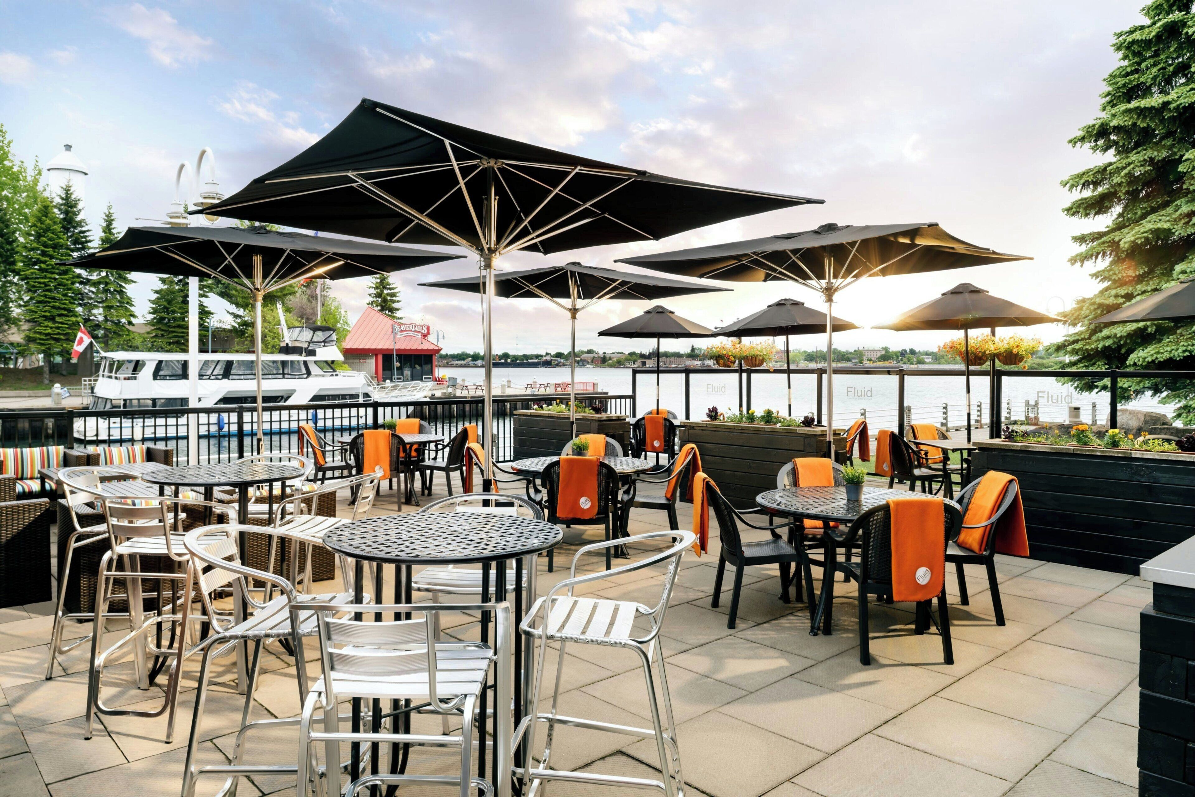 Une terrasse extérieure avec des tables et des chaises, des parasols et une vue sur l’eau.