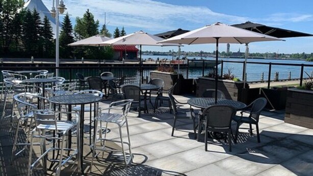 An outdoor patio with tables and chairs, overlooking a body of water and a city skyline. - Delta Hotels by Marriott Sault Ste. Marie Waterfront (Sault Ste. Marie)