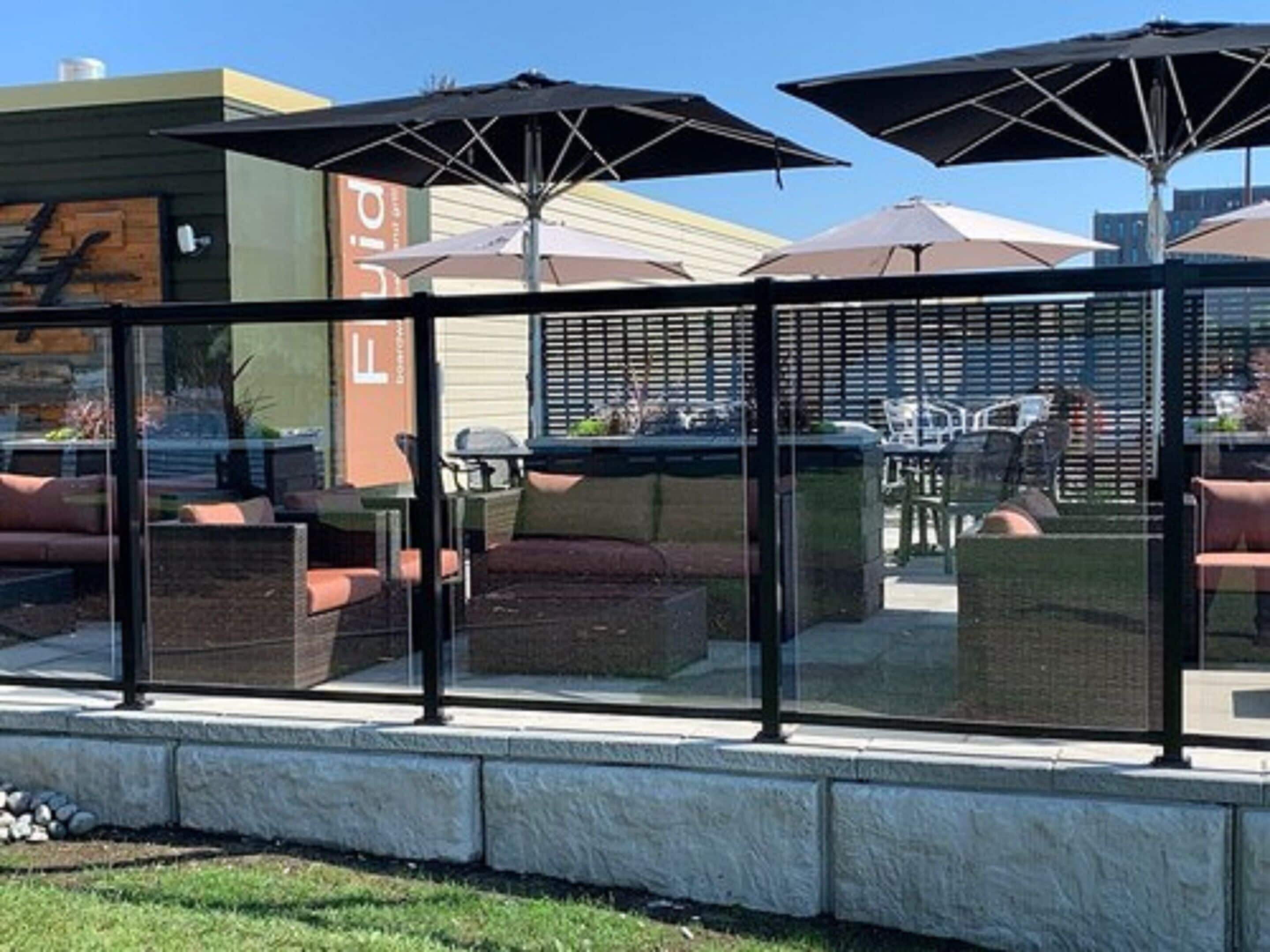 An outdoor seating area with glass partitions, outdoor furniture, and umbrellas.