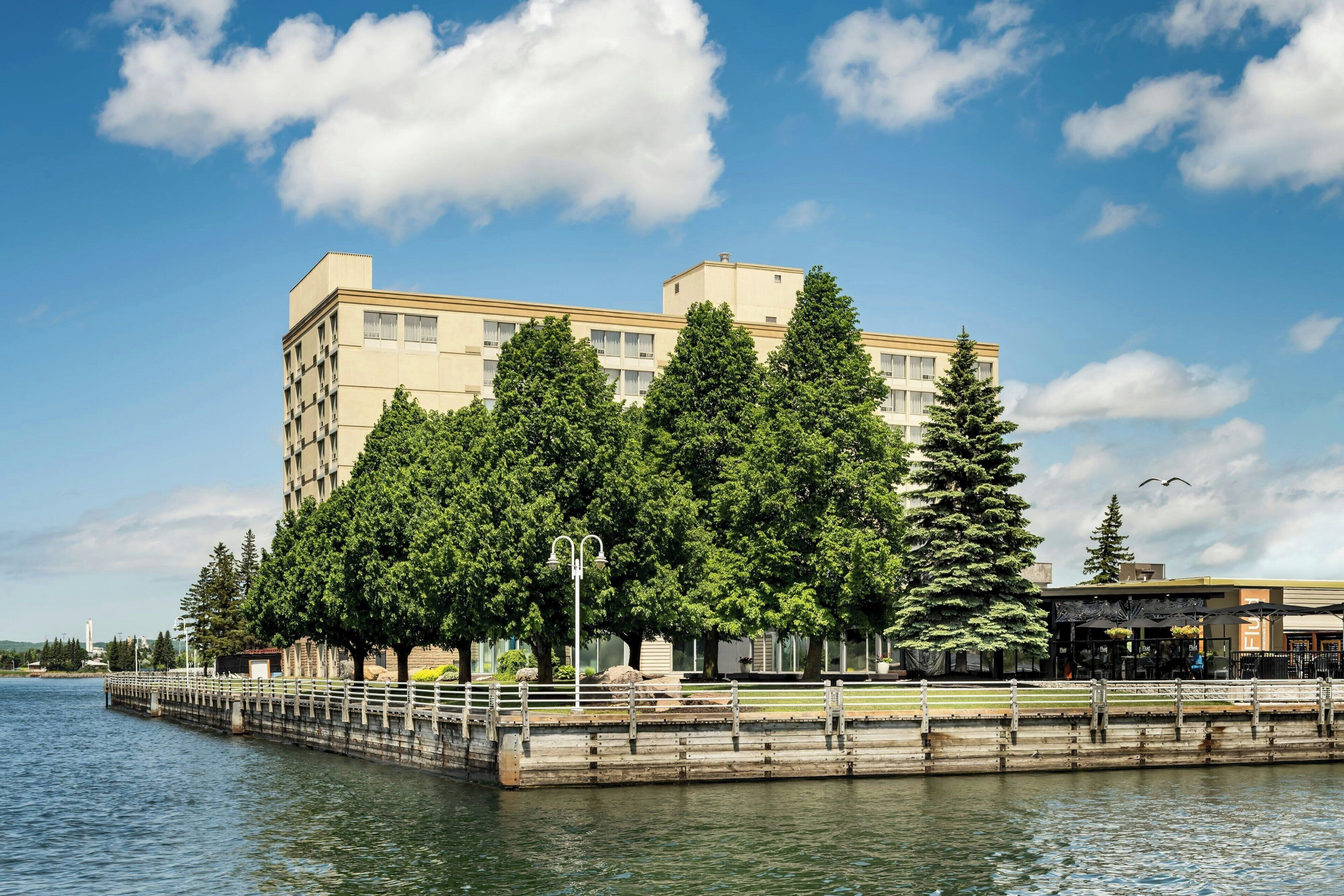 A hotel with a waterfront view, featuring a modern building, a dock, and lush greenery.