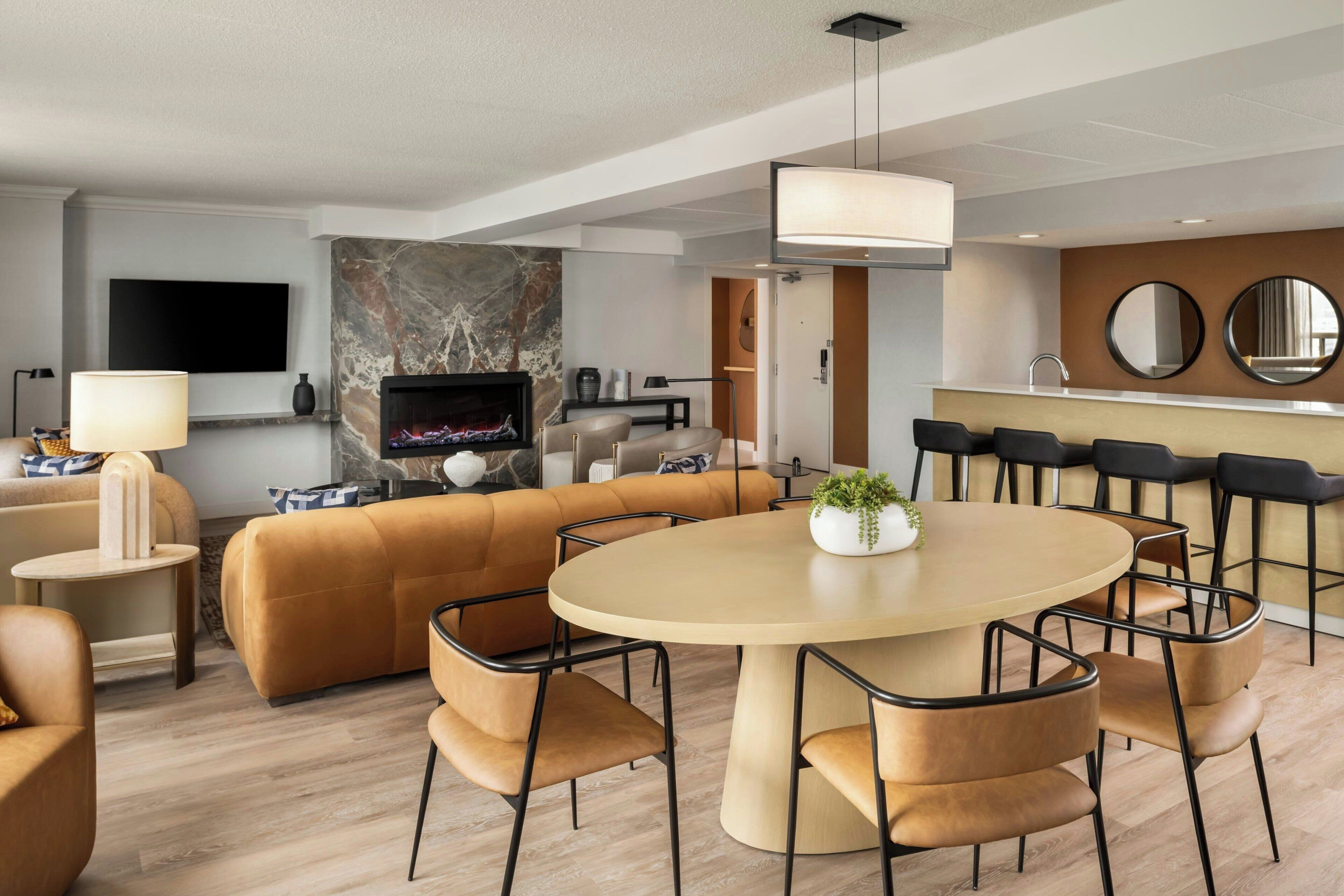 Una sala de estar moderna con chimenea, un sofá, una mesa de comedor con sillas, y una zona de cocina con barra.