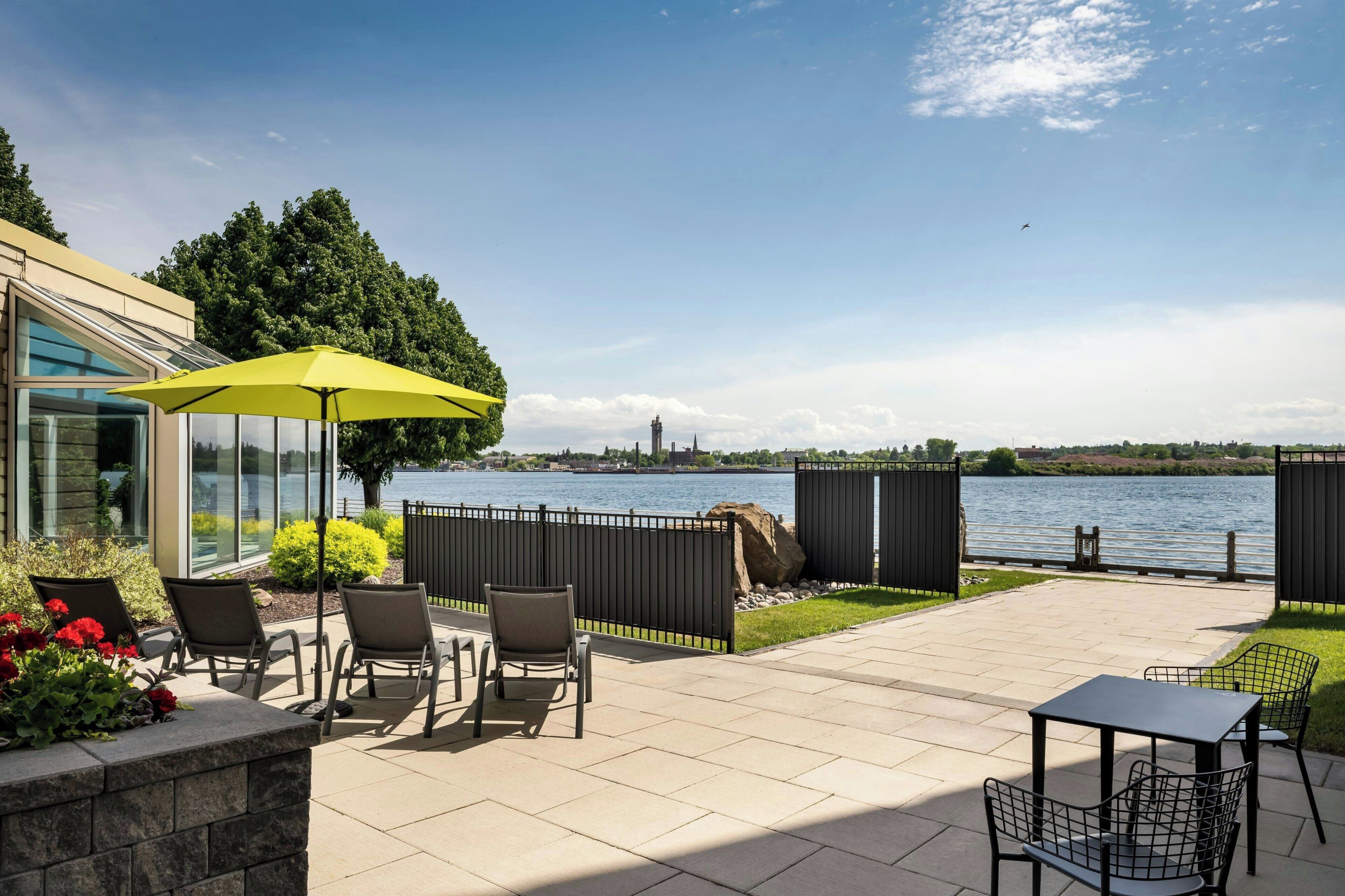 Un patio con mobili da esterno, un ombrellone giallo e vista sul fiume.