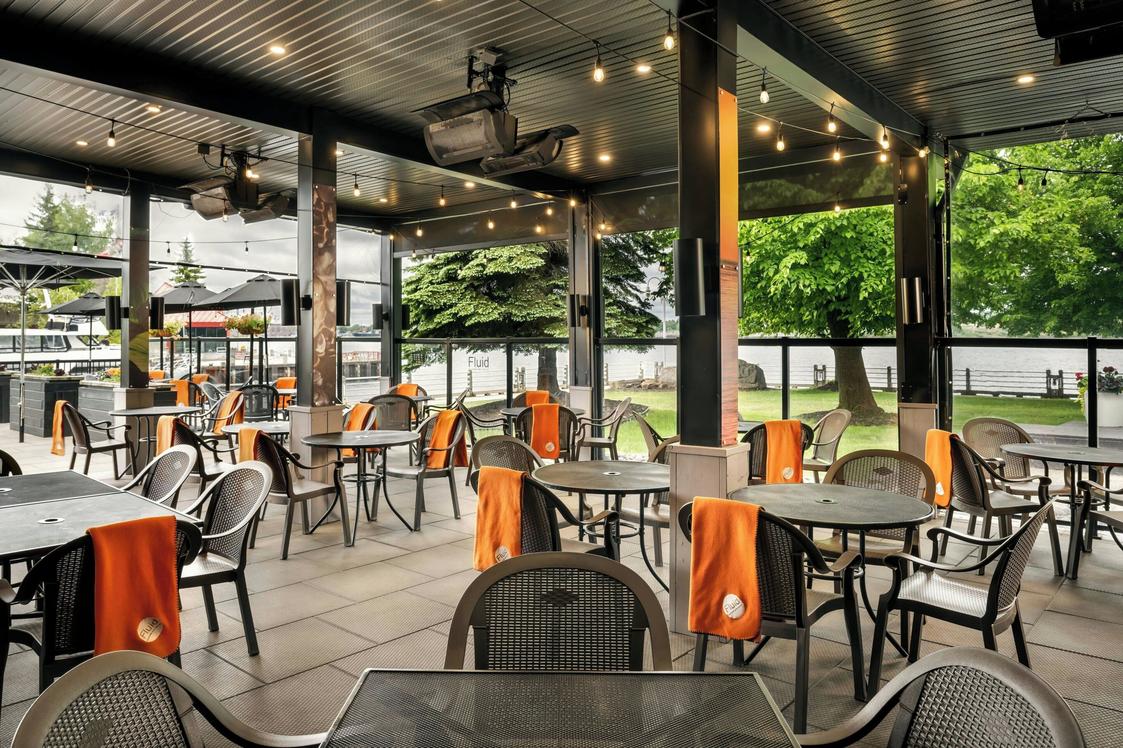 An outdoor seating area with tables and chairs, large windows, and a view of the water.