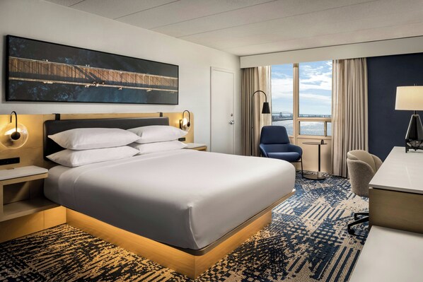A hotel room with a large bed, a desk, a chair, a desk lamp, a wall-mounted TV, and a window with a view of a bridge. - Delta Hotels by Marriott Sault Ste. Marie Waterfront (Sault Ste. Marie)