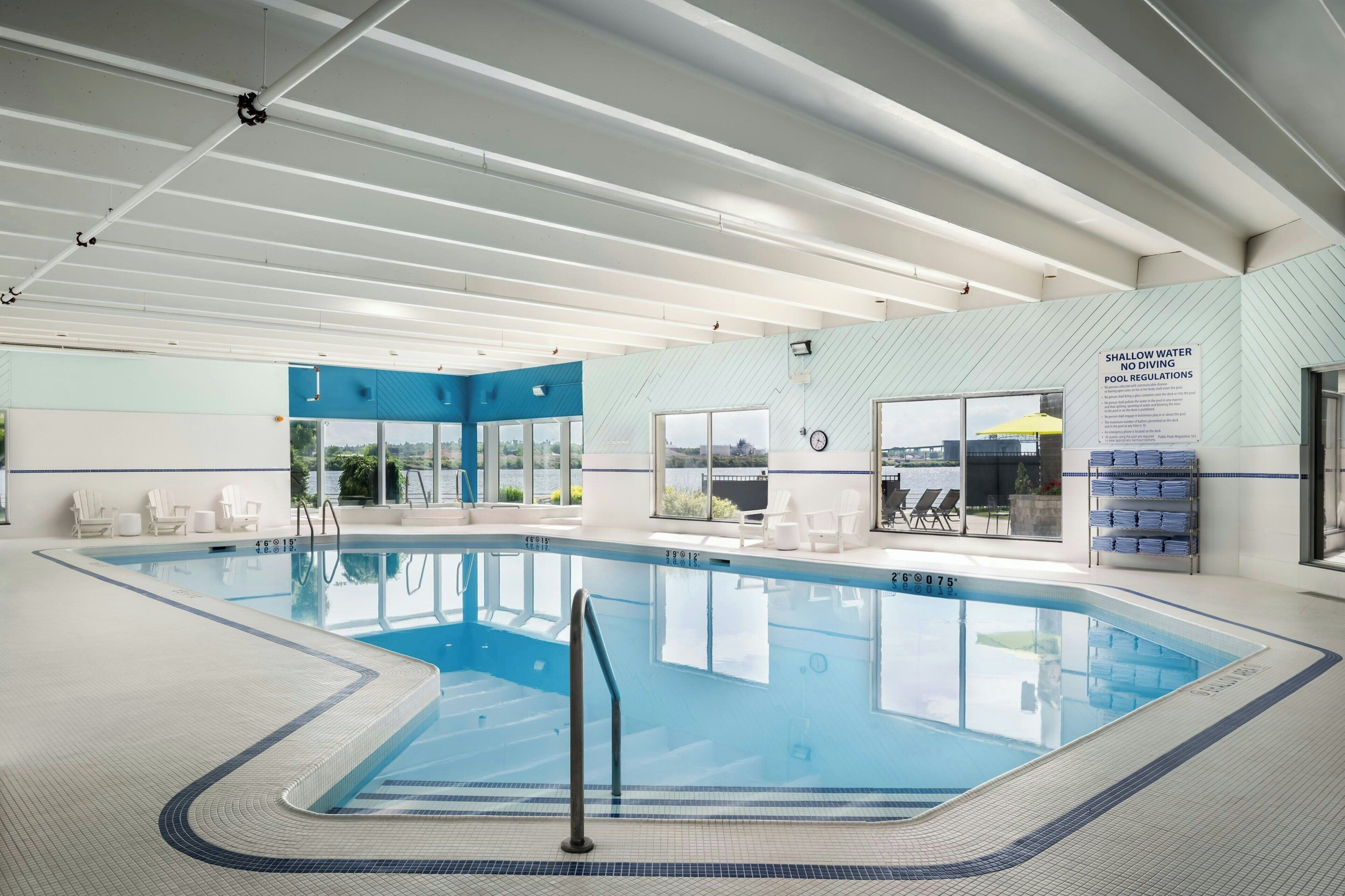 Ein heller, überdachter Pool mit klarem Wasser, umgeben von Liegestühlen und Blick ins Freie.