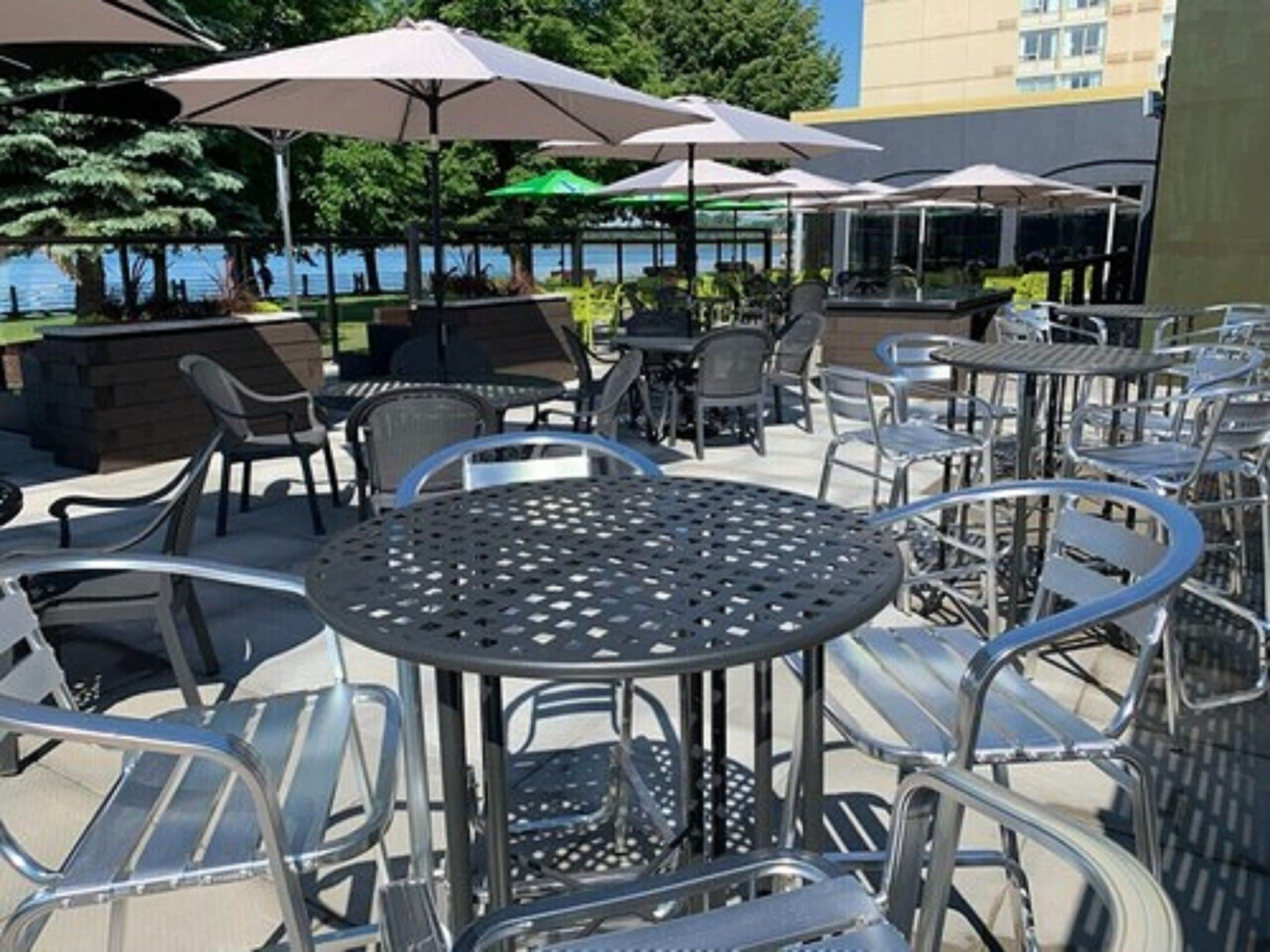 Outdoor seating with metal chairs and tables, umbrellas, and a view of a body of water.