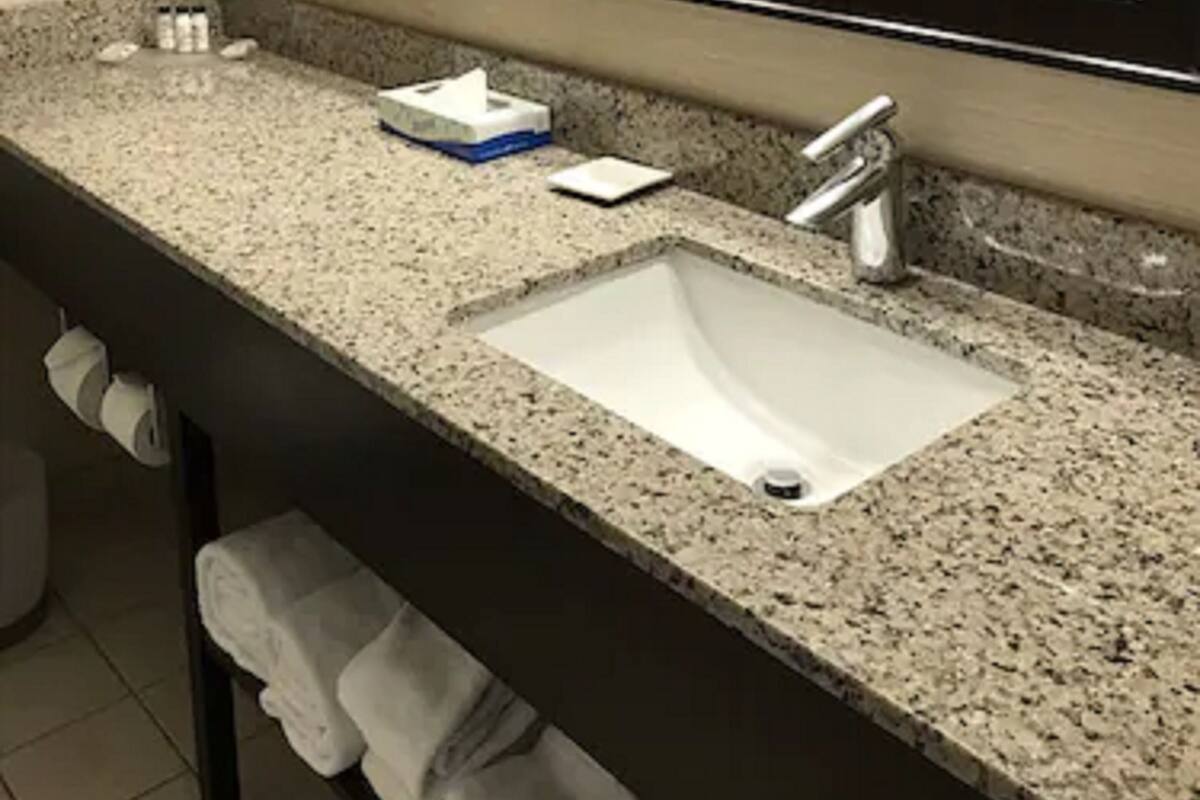 A bathroom with a granite countertop, a white sink, a large mirror, and framed pictures on the wall.