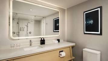 Uma casa de banho moderna com um espelho grande, chuveiro, sanita e lavatório com artigos de higiene pessoal.