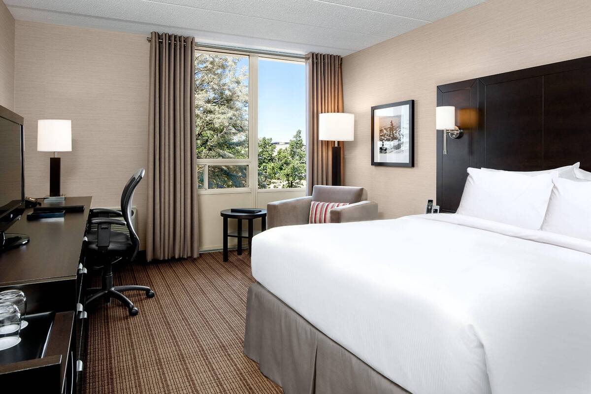 A hotel room with a large bed, a desk with a chair, a small table, and two lamps.