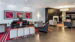 A modern living room with a sofa, armchairs, and ottomans, a fireplace, and framed artwork on the wall. - Delta Hotels by Marriott Sault Ste. Marie Waterfront (Sault Ste. Marie)