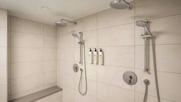 A modern bathroom with a shower area, including a handheld showerhead, a wall-mounted showerhead, and a handheld showerhead with a flexible hose. There are also three bottles of shampoo and conditioner on the wall.