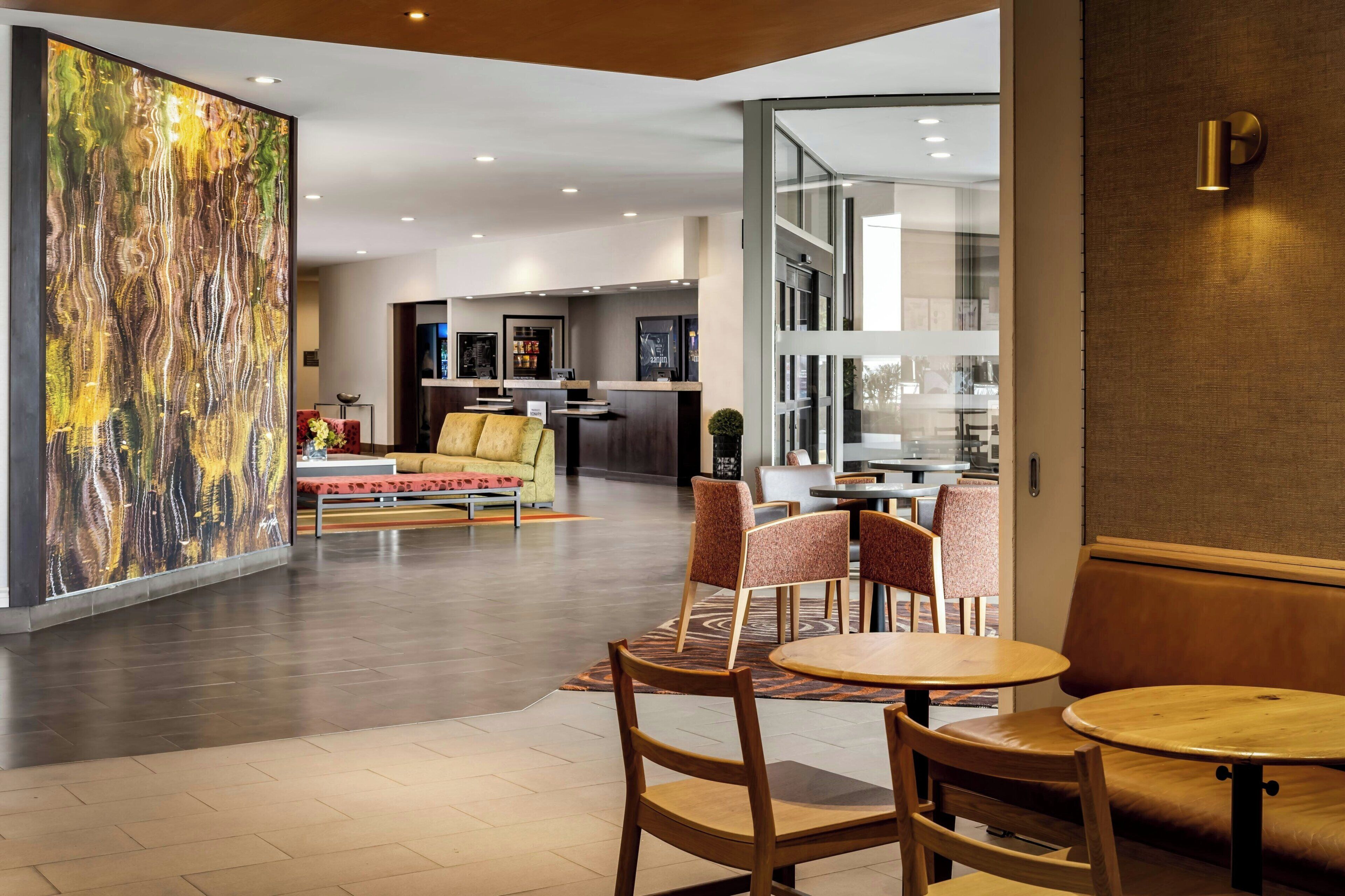 Een hotel lobby met een modern design, met een groot abstract schilderij, een zithoek met een bank en stoelen, en uitzicht op de eetruimte.